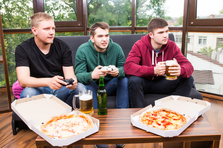 Young men drink beer, eat pizza and play video games  at homeの写真素材