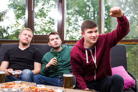 Young men drink beer, eat pizza and play games consoleの写真素材