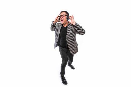 Showman concept. Middle age man listen music on headphones and sing song on whiteの写真素材