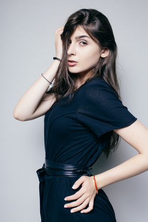 Young brunette lady in black dress posing on grey backgroundの写真素材