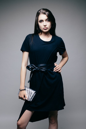 Young brunette lady in black dress posing on grey backgroundの写真素材