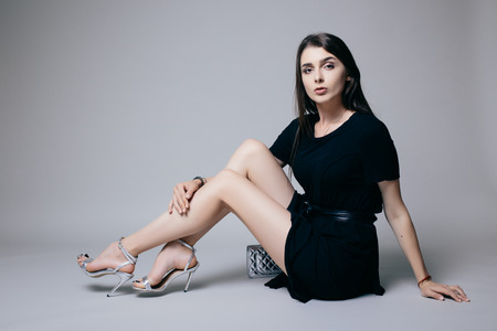 Beauty brunette girl sitting down and possing on grey background. Fashion photo.の写真素材