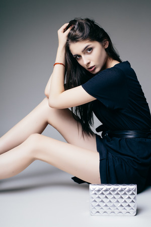 Beauty brunette girl sitting down and possing on grey background. Fashion photo.の写真素材