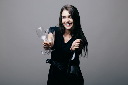 Girl with champagne bottle and drink glass pointed on you on grey background.の写真素材