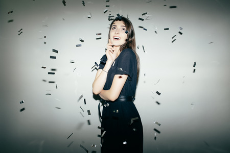 Happy young woman or teen girl in black dress  and confetti at partyの写真素材