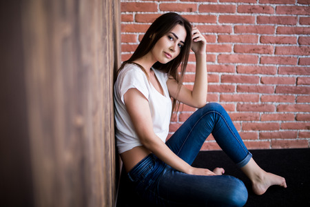 Girl sitting down against wooden and brick wallの写真素材