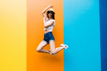 Jump of  pretty woman  cup in sunglasses and hat over  color wall backgroundの写真素材