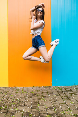 Jump of  pretty woman  cup in sunglasses and hat over  color wall backgroundの写真素材