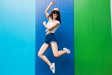 Jump of  pretty woman  cup in sunglasses and hat over  color wall backgroundの写真素材