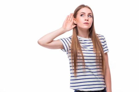 Young woman with a hearing disorder or hearing loss cupping her hand behind her ear with her head turned aside to try and amplify and channel the available sound to her ear drumの写真素材