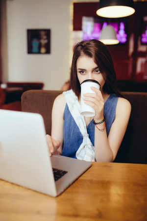 outdoor portrait of a young girl she works as a freelancer in a cafe drinking a delicious hot Cup of coffee from text send mail loads the photo freelancerの写真素材