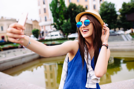 Young smiling teen happy woman making selfie on the street, glasses, traveling alone, having fun, positive mood, joy, vacation, surprised emotions. Urban life concept.の写真素材