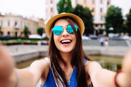 Young girl take selfie from hands with phone on summer city street. Urban life concept.の写真素材