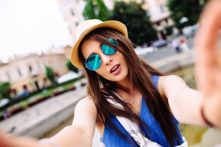 Young girl take selfie from hands with phone on summer city street. Urban life concept.の写真素材