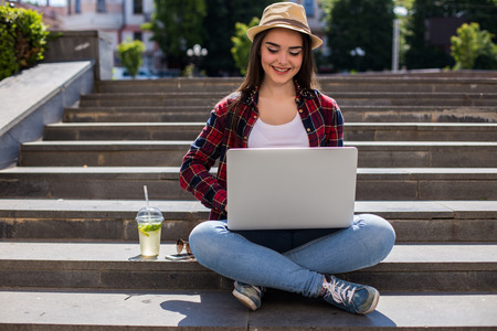Portrait of a happy young woman sitting on the city stairs and using laptop computer outdoorsの写真素材