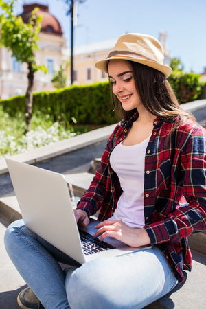 Portrait of a happy young woman sitting on the city stairs and using laptop computer outdoorsの写真素材