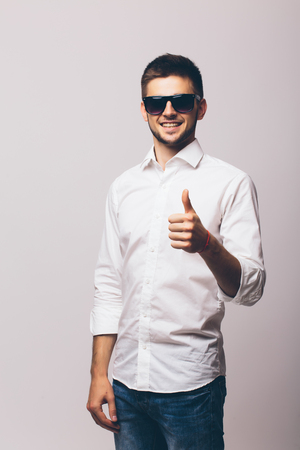 Handsome businessman in sunglasses pointing at camera over grey backgroundの写真素材