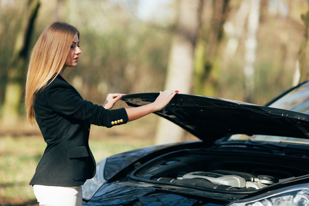 A woman waits for assistance near her car broken down on the road side.の写真素材