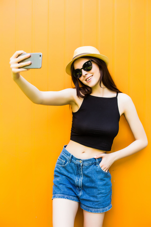 Smiling summer woman take selfie with hat and sunglasses over bright background.の写真素材