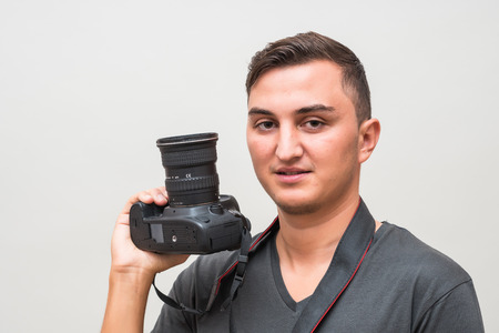 Portrait of a happy handsome man holding camera isolated on a gray background