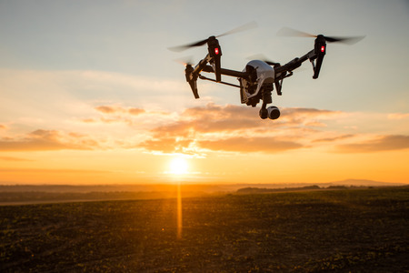 White drone with digital camera flying in sky over field on sunsetの写真素材
