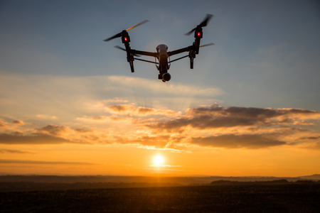 White drone with digital camera flying in sky over field on sunsetの写真素材