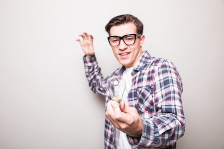 Astonished young man in glasses holding small light bulb