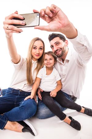 Happy family on white background. Mother, father and daughter take selfie on phoneの写真素材