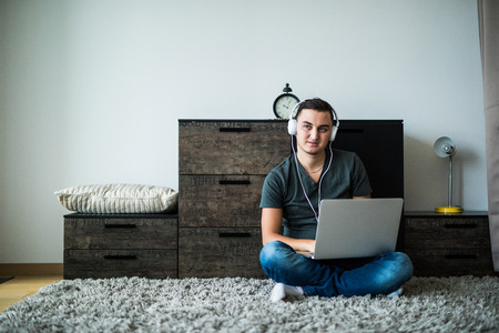 Young man use laptop and listen headphones on carpet at homeの写真素材