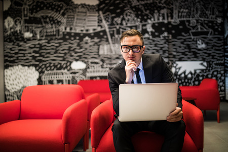 young businessman in eyeglasses working on laptop while sitting in officeの写真素材