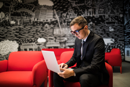 Side view of confident young man in eyeglasses working on laptop while sitting in officeの写真素材