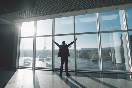 Business man celebrate victory and success in work alone against panoramic windowsの写真素材