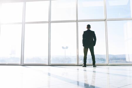 Sihluette of young businessman against big panoramic windowsの写真素材