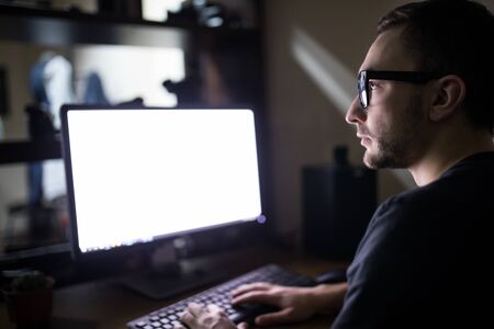 Young man work on PC. White screen of monitor.