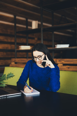 Business lady speak on phone and make notes at work table in office hubの写真素材