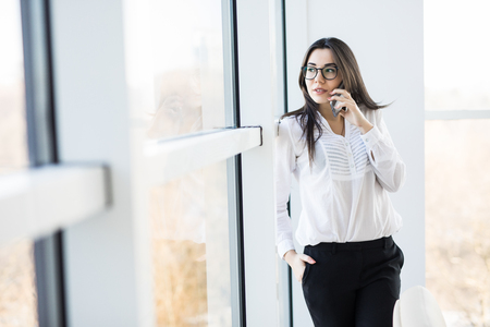 Business woman speak on phone near big office windows in modern smart space.の写真素材
