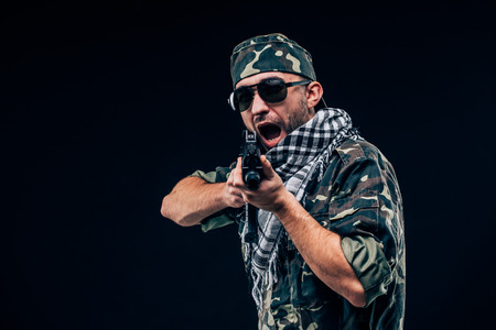 Terrorist atack. Portrait of Terrorist with gun and sunglases over dark backgroundの写真素材