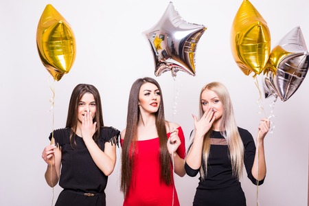 Three lovely young women standing and holding star shaped balloons over white backgroundの写真素材