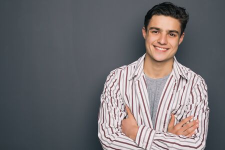 Happy smiling cheerful guy with crossed hands on gray backgroundの写真素材