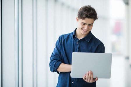 Handsome young man man holding and use a laptop in hallの写真素材