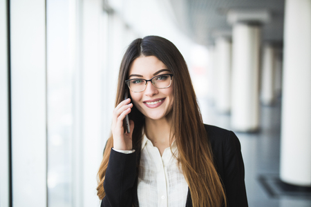 Young woman with mobile phone in the office against panoramic windowsの写真素材