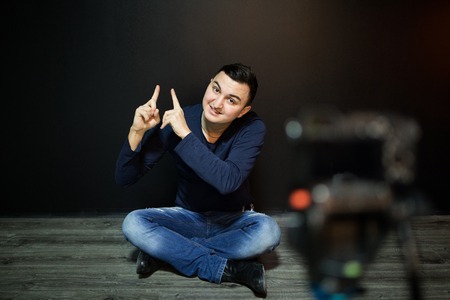 Man in focus on digital camera LCD screen waving hand while seated on ground against wall for concept about video bloggingの素材 [FY31072971424]