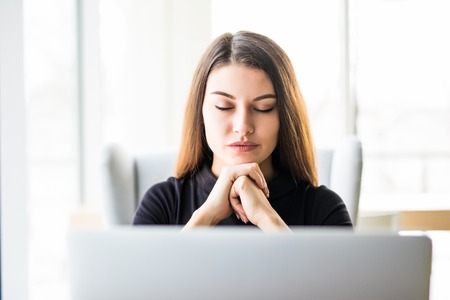Business woman resting chin on hand in front of her laptop at officeの写真素材