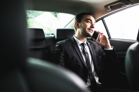 Businessman on call in car, smiling on passanger seatの写真素材
