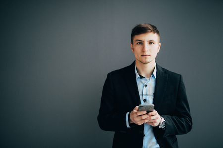 Smiling businessman leaning against a wall while using the smartphoneの写真素材