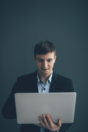 Handsome young businessman is using a laptop, looking at camera and smiling on black backgroundの写真素材