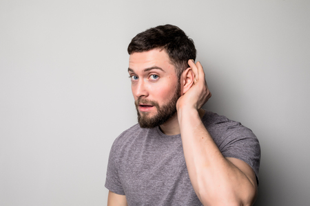 Closeup portrait a man placing hand on ear listening carefully to gossip isolated on gray wall...