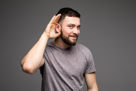Listening male holds his hand near his ear over grey background. Handsome man trying to listen to the conversation of someone.の写真素材