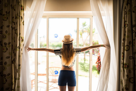 girl opens the curtains, Summer morning in hotel roomの写真素材
