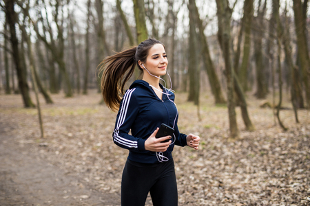 Young woman with headphones jogging in park and looking to mobile phoneの写真素材